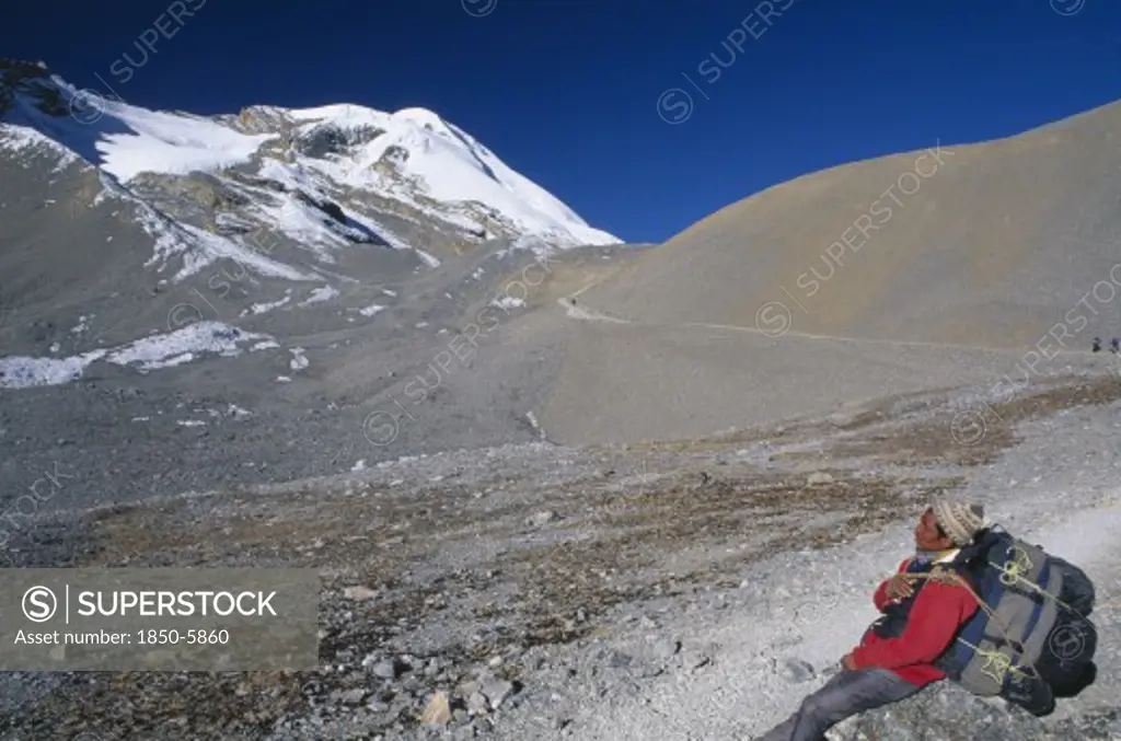 Nepal, Annapurna , Porter Carrying Large Back Pack Resting On The Approach To Thorung La Pass.