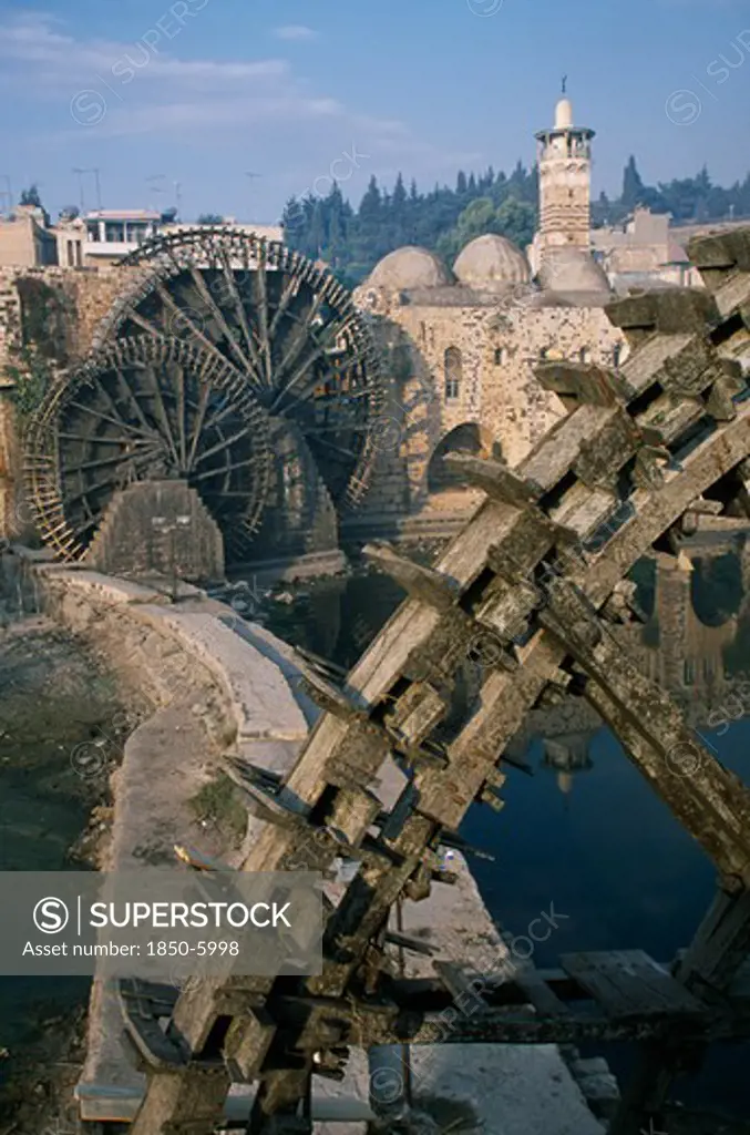 Syria, Central, Hama, Wooden Norias Or Waterwheels On The Orontes River And The Al-Nuri Mosque Dating From 1172 And Built Of Limestone And Basalt.  Large Section Of A Wheel In The Immediate Foreground.