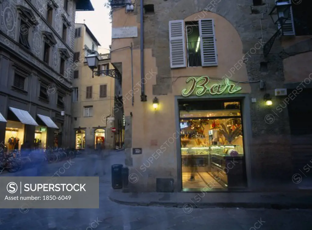 Italy, Tuscany, Florence, Ice Cream Bar With Neon Sign Illuminated At Night In Narrow Street With Pedestrians In Blurred Movement.