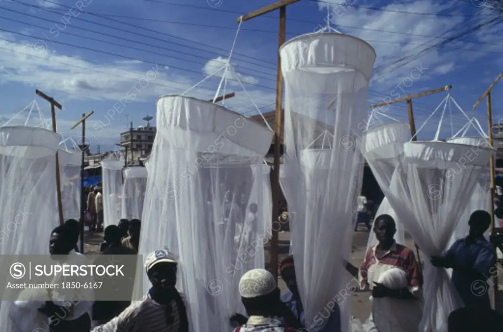 Tanzania, Dar Es Salaam, Mosquito Nets For Sale At Market With Men In The Foreground And Seen Through The Nets.