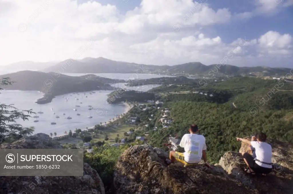 West Indies, Antigua, General, Couple Sitting On Rocks On Hillside Above Ordnance Bay On The Right And Tank Bay On The Left.
