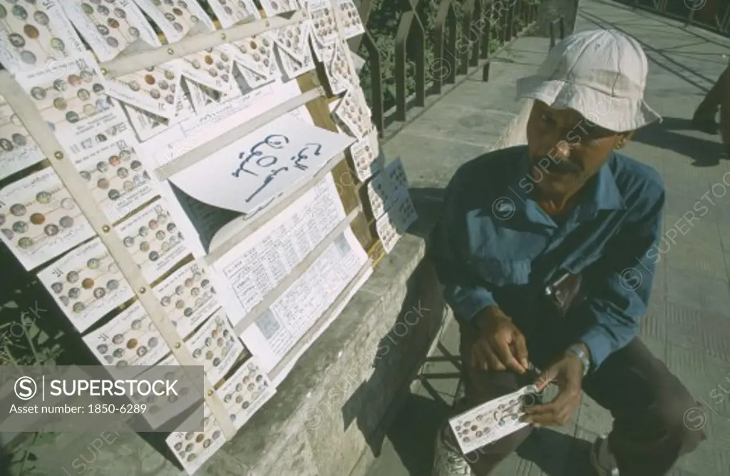 Syria, Damascus, Local Street Vendor Selling Lottery Tickets On The Side Of A Path.
