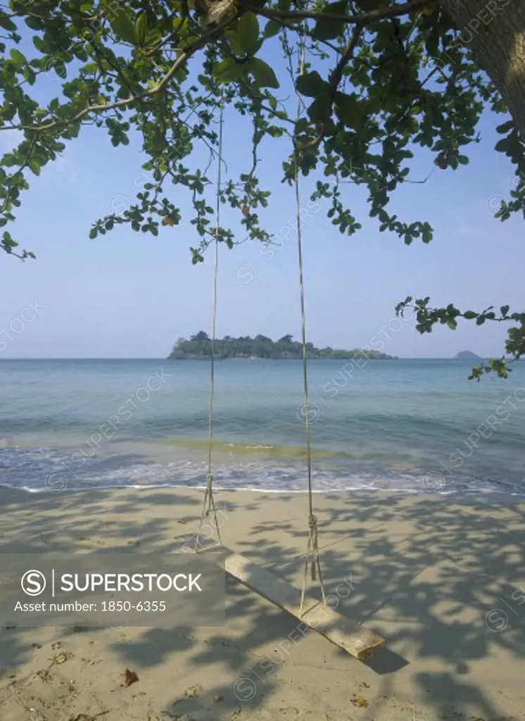Thailand, Trat Province, Koh Chang, Kai Bae Beach View From Sandy Beach Out Towards Koh Man Nai Island With Wooden Swing In The Foreground Hanging From Trees Overhead.