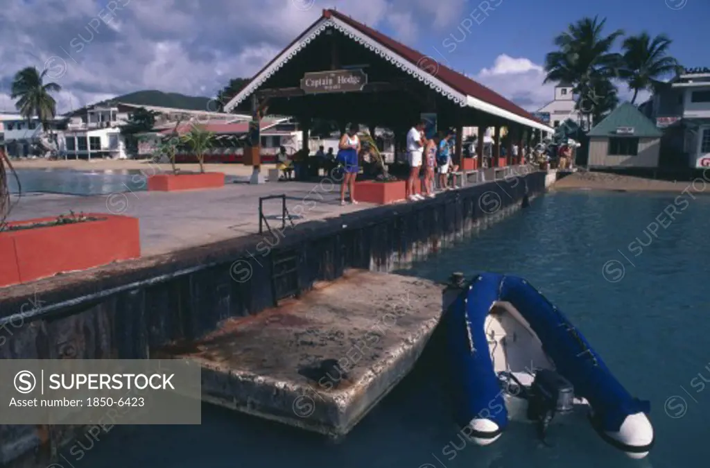 West Indies, Dutch Antilles, St Maarten, Philipsburg.  Quayside With Tourists Looking In The Water And The Captain Hodge Wharf Behind.  Dingy Moored In The Foreground.