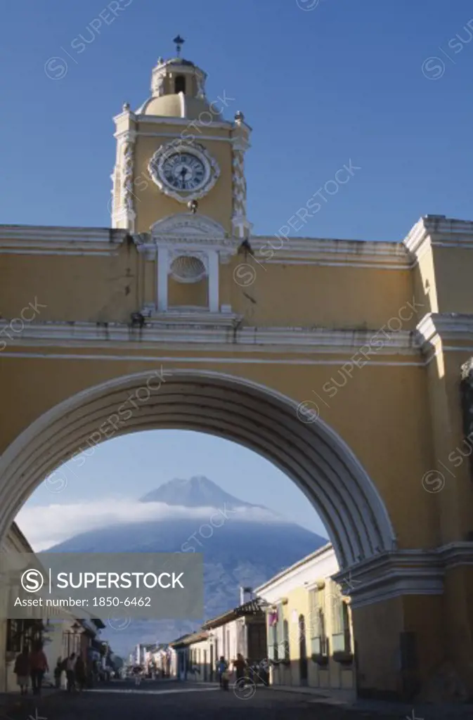 Guatemala, Antigua, 'Arco De Santa Catarina. Yellow Painted Archway With Clock Tower And People Walking, With Volcan Agua Visible Through Arch.'