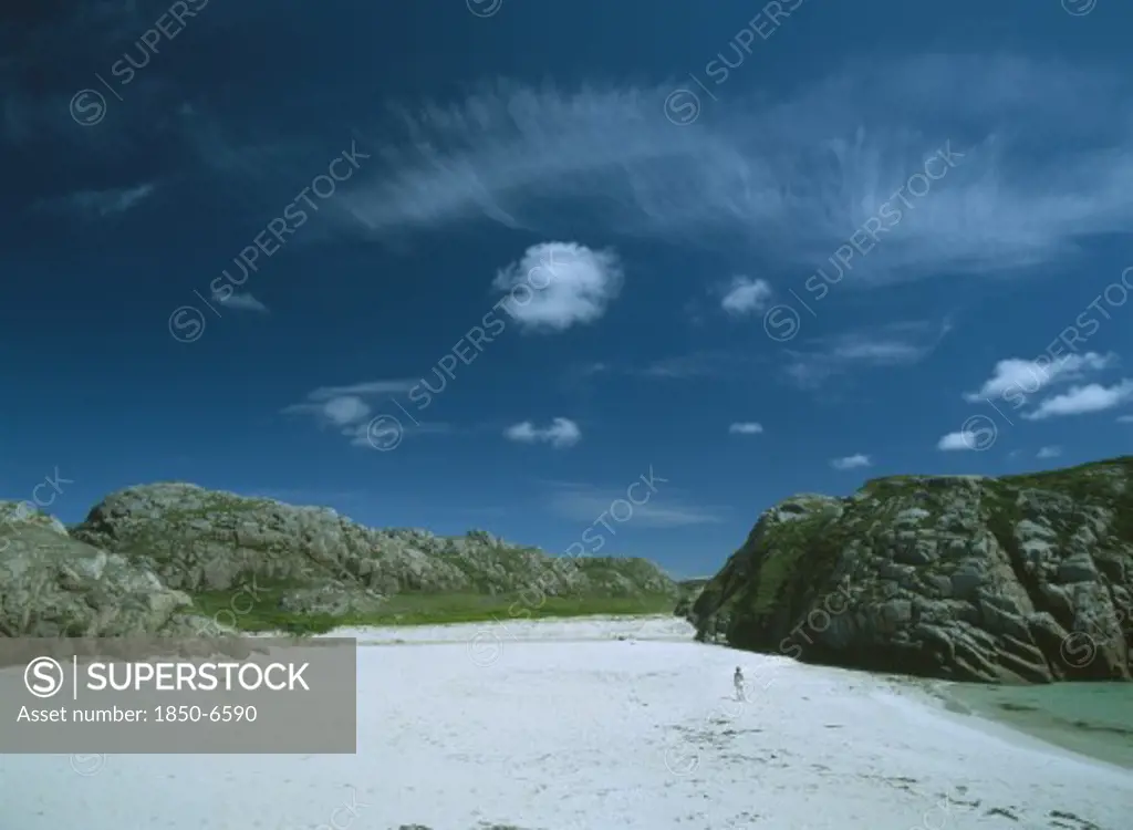 Scotland, Strathclyde, Isle Of Mull, White Sand Beach With Large Moss Covered Bolders And A Woman Standing In The Distance