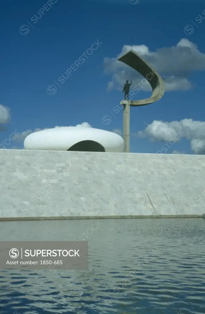 Brazil, Federal District, Brasilia, Kubitschek Memorial With Large Sculpture Holding A Statue Seen Over Surrounding Pool