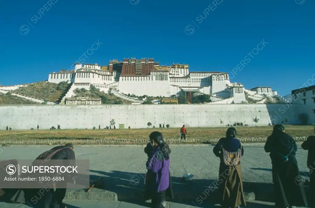 China, Tibet, Lhasa, Potala Palace On The Hillside With Row Of Pilgrims Prostrating Themselves In The Foreground.
