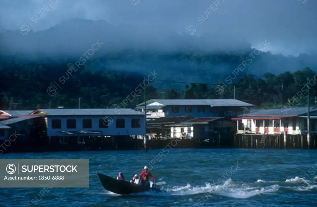 Brunei, Bandar Seri Begawan, Morning Mist Rising From The Jungle Behind The Kampong Stilt House Village With A Water Taxi On The River In The Foreground