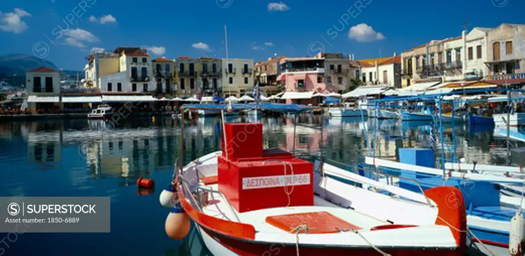 Greece, Crete, Rethymno, 'Venetian Port.  Colourful Red, White And Blue Painted Boats Moored In Harbour Overlooked By Hotels, Bars And Restaurants.'