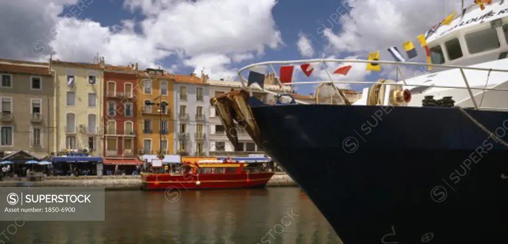France, Languedoc-Roussillon, Herault, Sete.  Part View Of Harbour And Colourful Waterside Buildings With Prow Of Boat Draped With Flags In The Foreground.