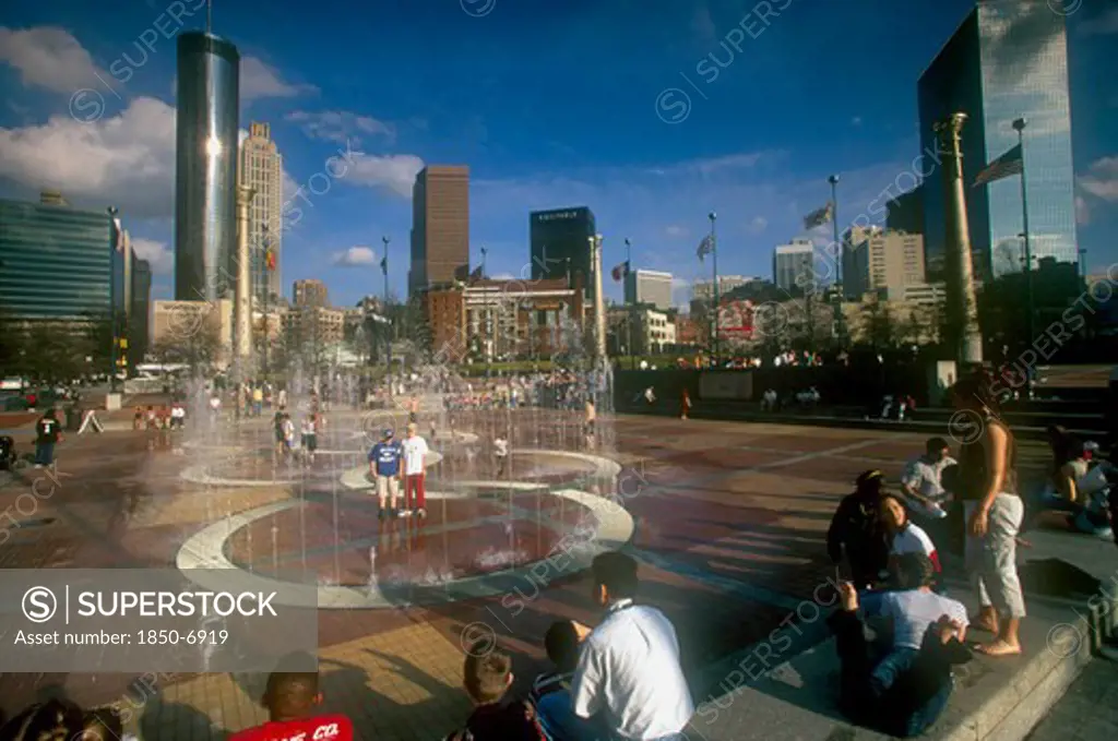 Usa, Georgia, Atlanta, 'Centennial Olympic Park.  Visitors Around Paved Area With Fountains, City Skyline Behind.'