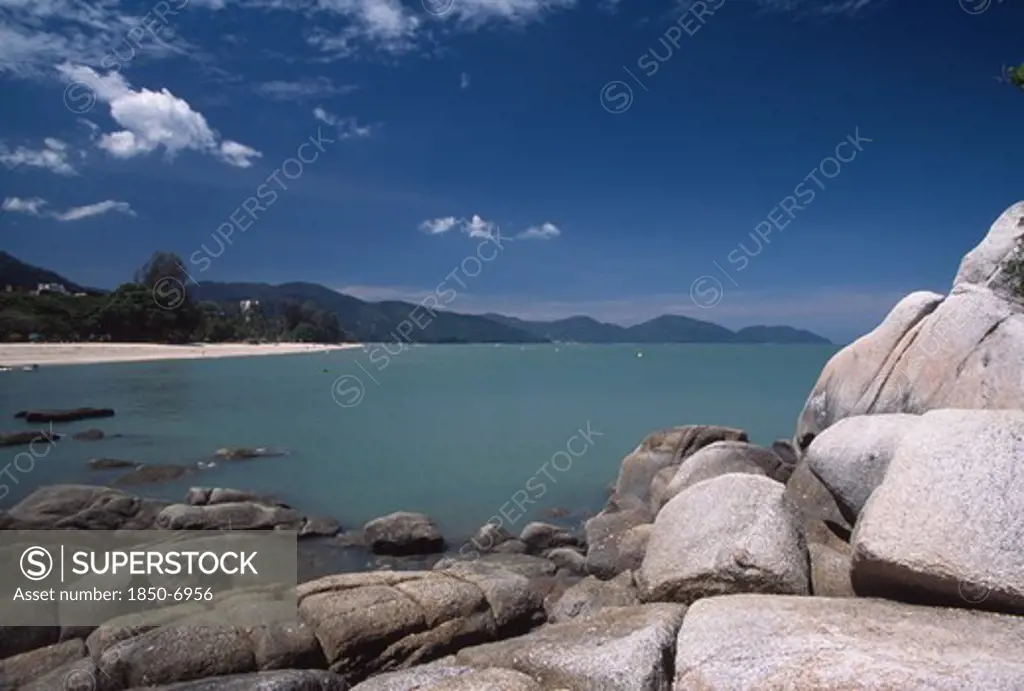 Malaysia, Penang, Batu Ferringhi, View Over Rocks And Bay Of Turquoise Water Towards Quiet Sandy Beach.