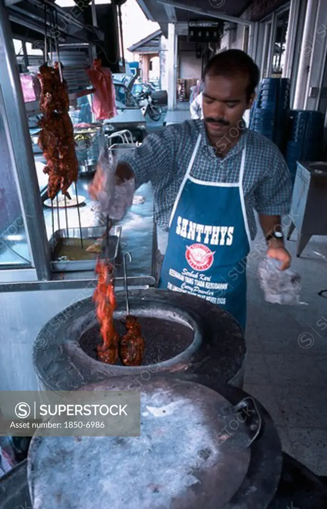 Malaysia, Penang, Georgetown, Man Cooking Tandoori Chicken In Circular Clay Oven At Roadside Stall Outside Kapitan Restaurant