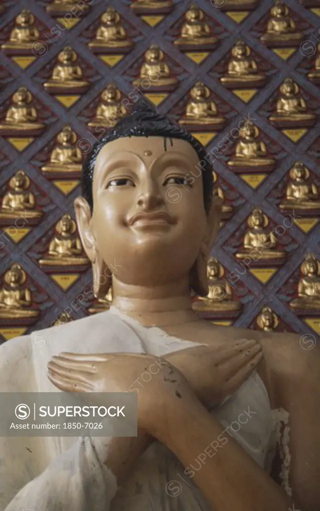 Malaysia, Penang, Georgetown, Wat Chayamangkalaram.  Detail Of Buddha Figure With Hands Crossed Over Chest.  Wall Behind Covered With Small Raised Seated Buddha Figures Painted Gold.