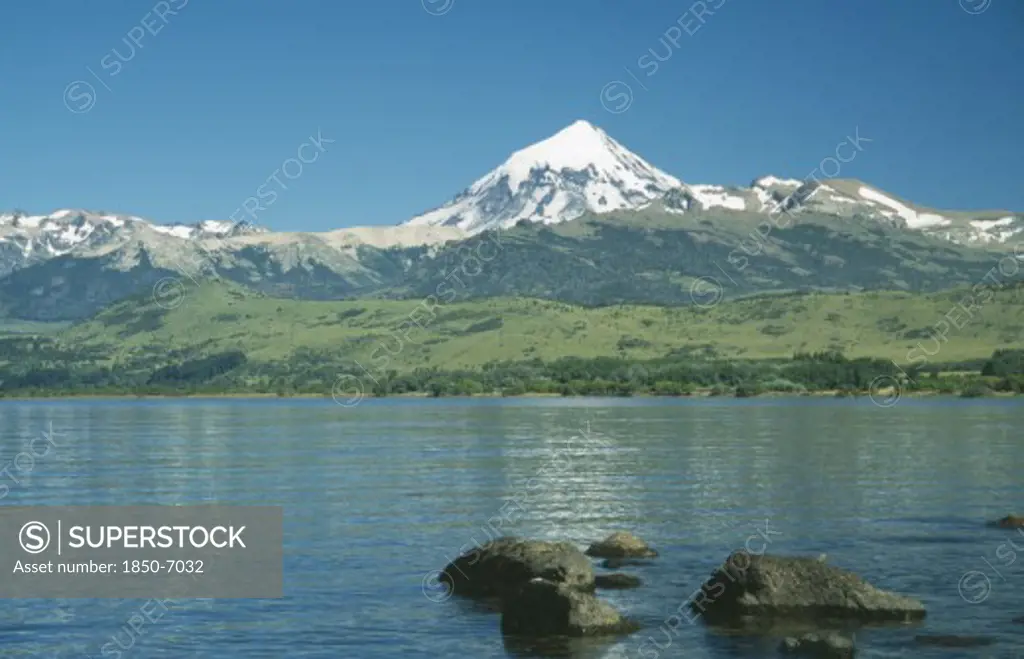Argentina, Neuquen, Lanin National Park, View Over Bolders Of Huechulafquen Lake Toward Snow Capped Lanin Volcano.