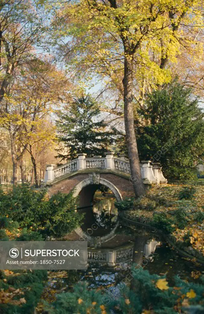 France, Ile De France, Paris, Parc Monceau Created By Landscape Designer Louis Carmontelle.  Arched Bridge Over Stream Surrounded By Trees.