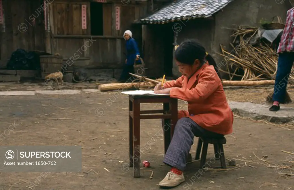 China, Guizhou, Young Girl Doing Homework At Desk In Farmyard.