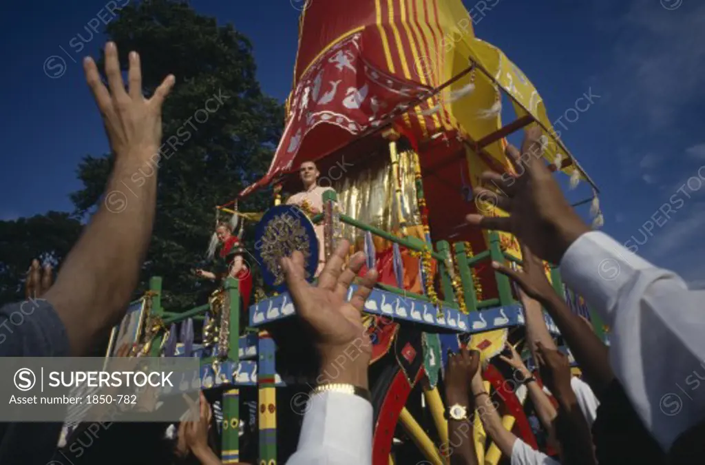 Religion, Hare Krishna, View Over The Reaching Hands Of A Crowd Toward Brightly Decorated Cart With Two People Standing On The Top During A Festival