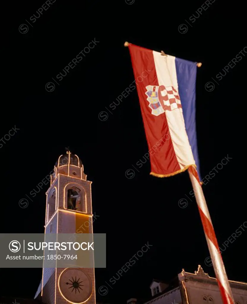 Croatia, Dalmatia, Dubrovnik, View Looking Up At The Clocktower Illuminated At Night With Croatian Flag In The Foreground