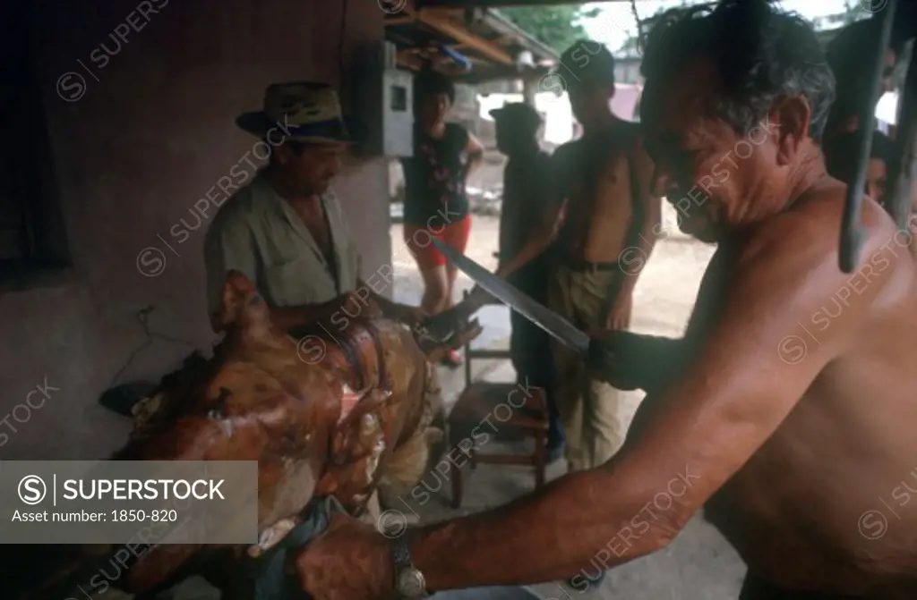 Cuba, Palma Soriano, Man Standing At Spit Carving A Whole Roasted Pig With A Large Knife