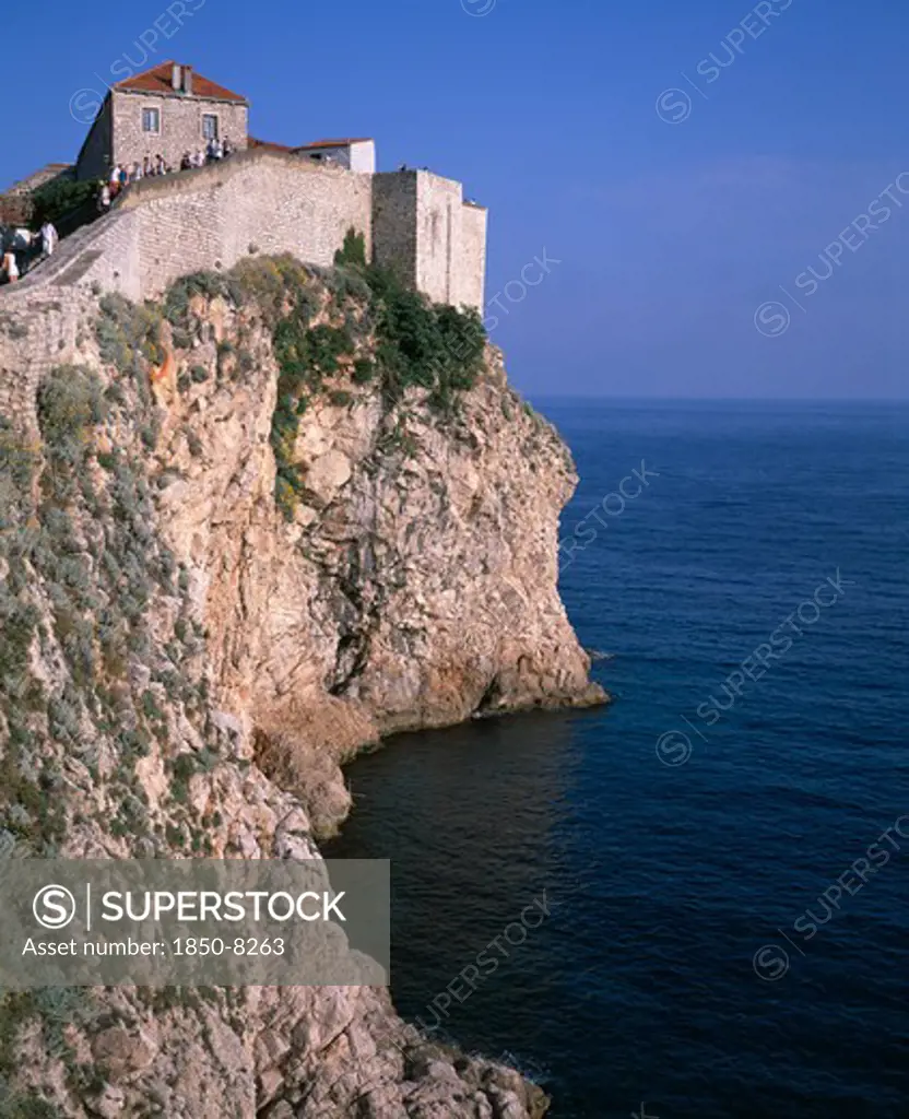 Croatia, Dalmatia, Dubrovnik, Tourists Climbing The City Walls Atop A Rocky Cliff Overlooking The Adriatic Sea