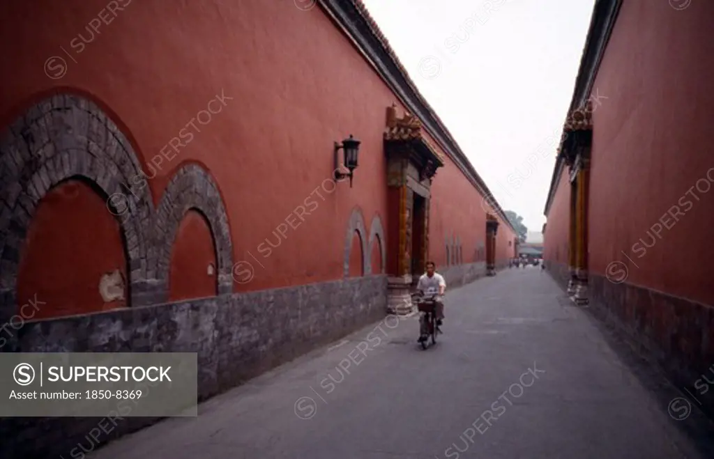 China, Beijing, The Forbidden City.  Cyclist On Narrow Street Between Red Painted Walls.