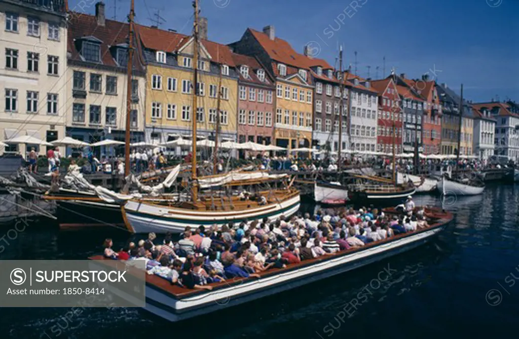 Denmark, Zealand, Copenhagen, Nyhavn Canal. Cruise Boat Passing Sailing Boats Moored On The Quayside Beside Brightly Painted Traditional Houses