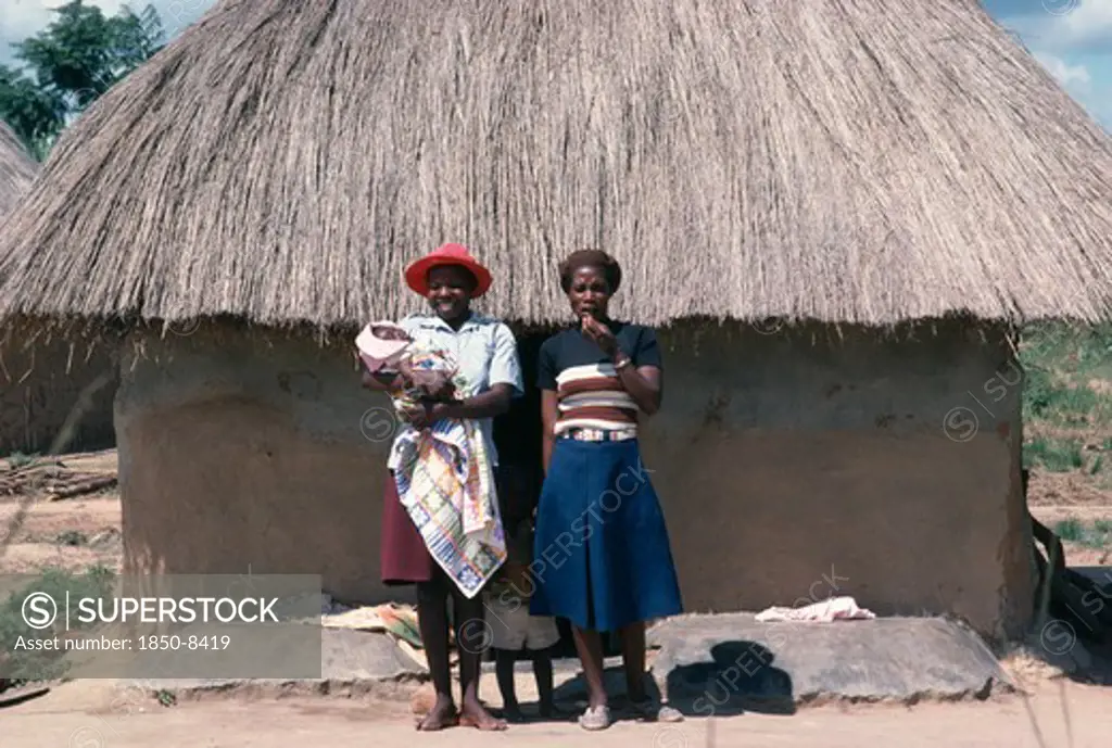 Zimbabwe, General, Young Shona Women And Children Standing Outside Thatched Hut.