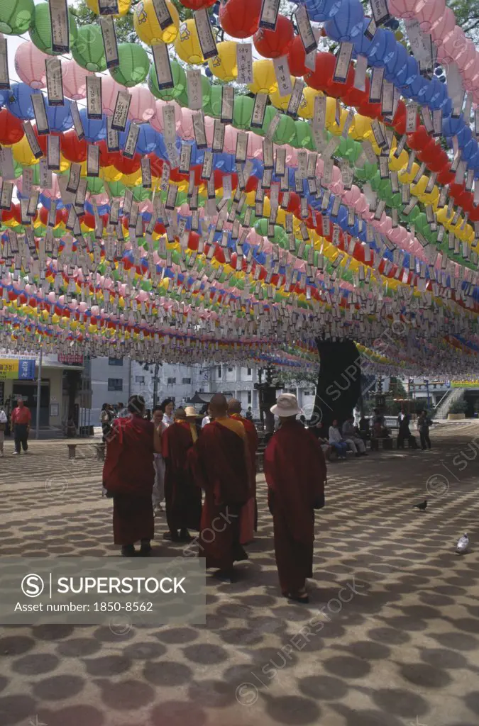 South Korea, Seoul, Jogyesa Temple.  Canopy Of Paper Lanterns And Prayer Streamers Hung To Celebrate The Birthday Of Buddha With Group Of Tibetan Buddhist Monks Standing Below.