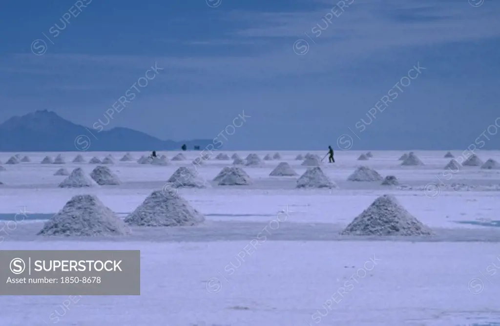 Bolivia, Altiplano, Salar De Uyuni, View Over The Salt Plains With Figure Sweeping Up Piles Of Salt For Extraction