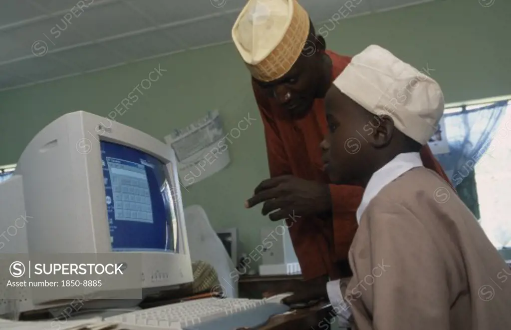 Nigeria, Education, Teacher Leaning Over Boy Sitting At A Computer In A Classroom
