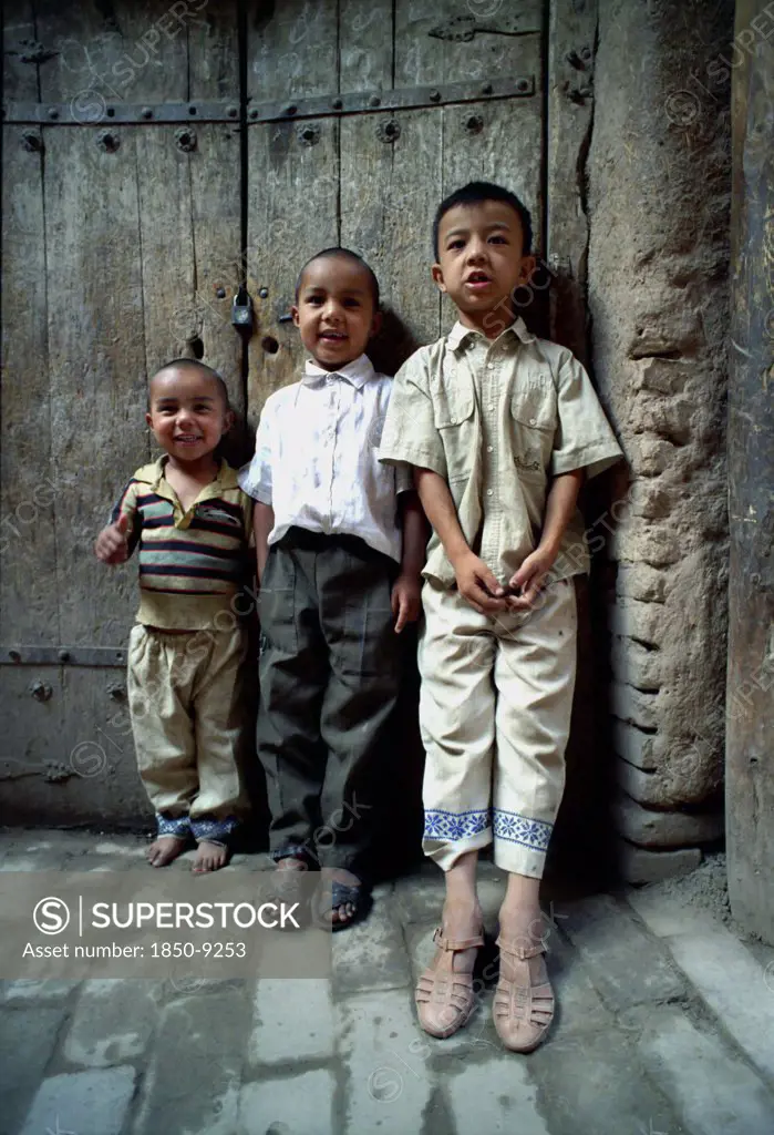 China, Xinjiang, Kashgar, Three Young Boys Standing Against A Wooden Door On A Cobbled Street