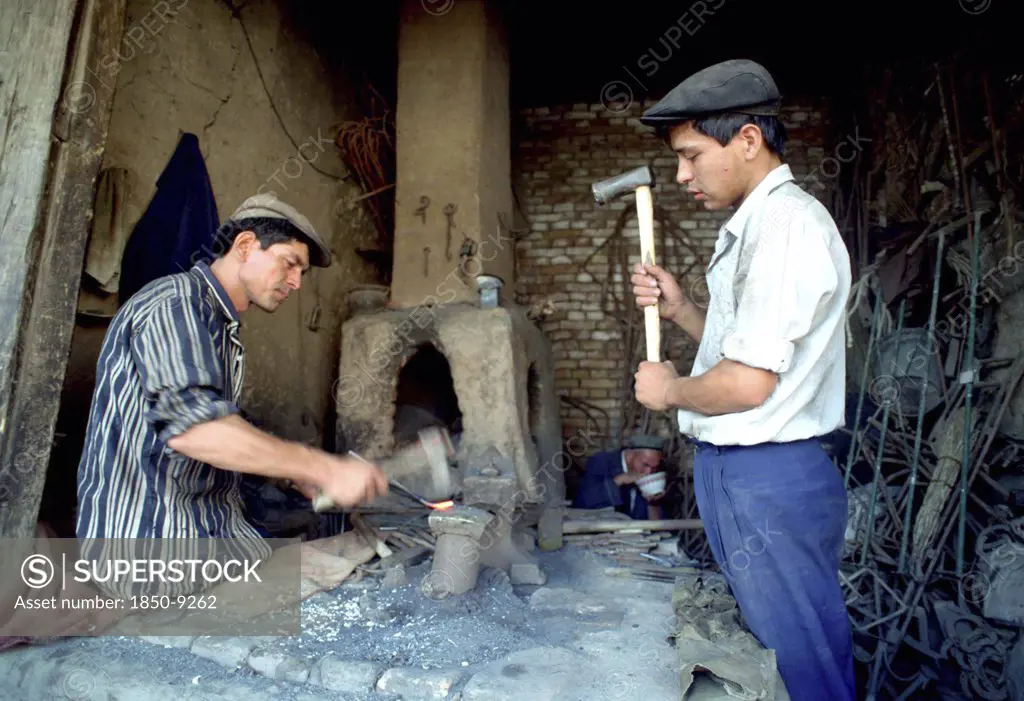 China, Xinjiang, Kashgar, Blacksmith Beating Heated Metal In His Workshop With Helper