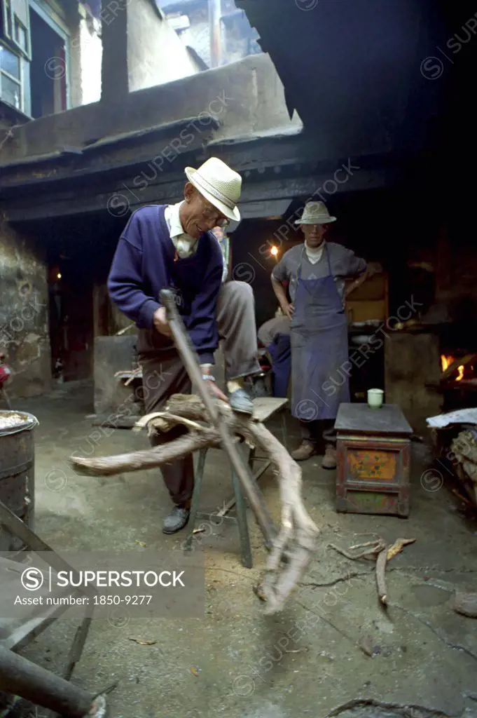 China, Tibet, Lhasa, Elderly Man Cutting Firewood For The Kitchen In A Courtyard