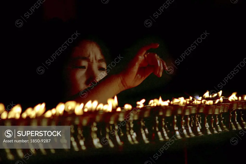 China, Tibet, Lhasa, Jokhang Temple. Woman Lighting Prayer Lamps Fueled With Yak Butter