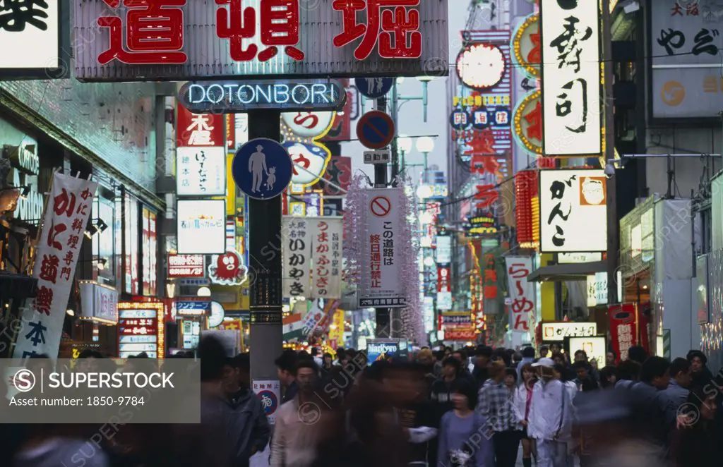 Japan, Honshu, Osaka, Dotonbori Sign Illuminated At Dusk Among Mass Of Other Neon Signs With Crowds Of Shoppers Below