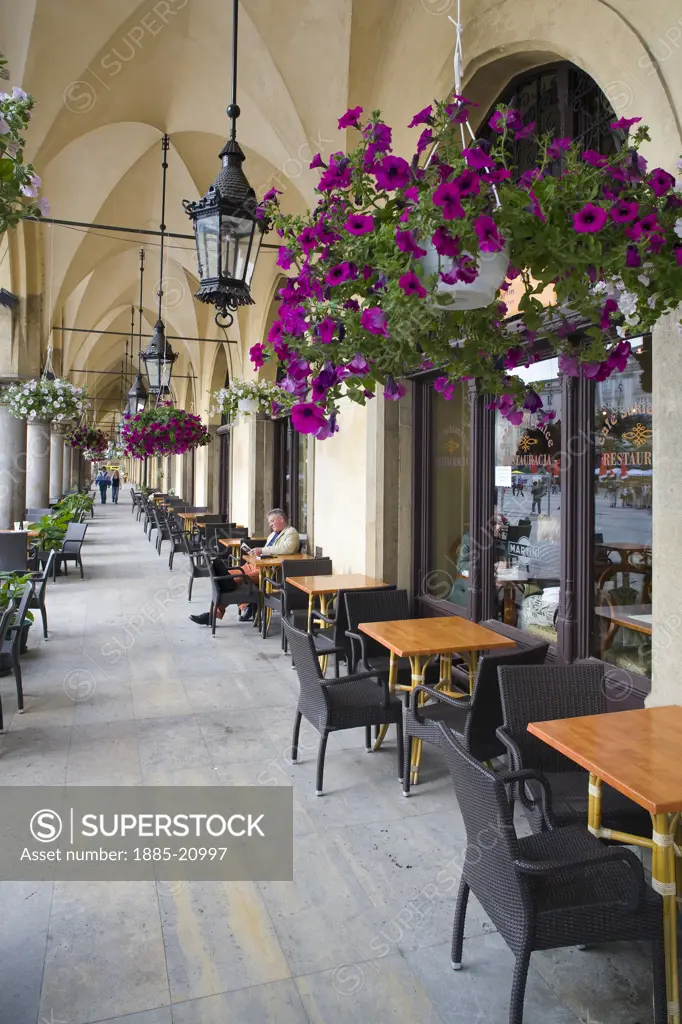 Poland, Krakow, Colourful flowers and hanging baskets outside a cafe on a arched walkway outside the Cloth Hall or Sukiennice in Krakow