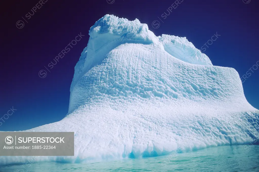Antarctica, Antarctic Peninsula, Curved ice formation - with blue ice glow and green blue water at base and deep blue skies