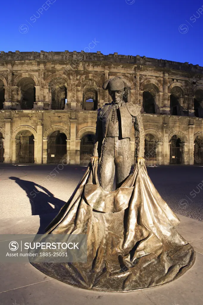 France, Languedoc-Roussillon, Nimes, Place des Arenes - amphitheatre and matador statue at night