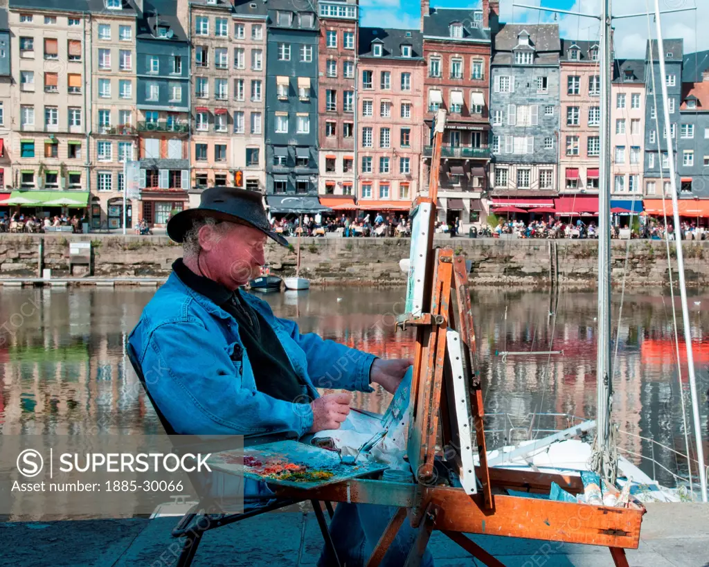 An artist working at his easel on the quayside in Honfleur, Normandy, France.