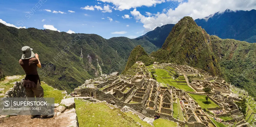 Taking in the overview of Machu Picchu from the upper terraces outside the city, a lone woman uses her camera to capture the ancient ruins.