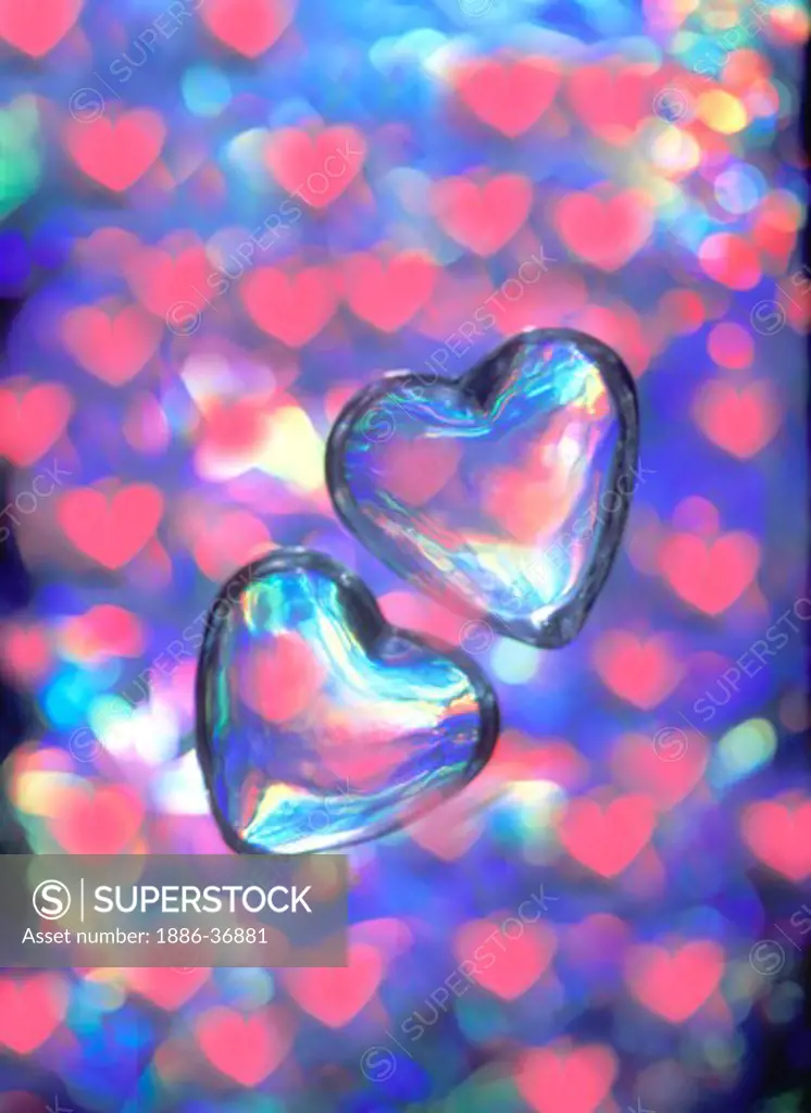 Two floating transparent glass hearts with small pink hearts in background.