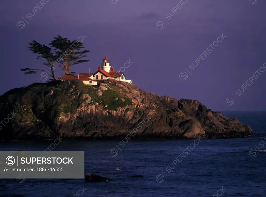Battery Point Lighthouse on a tidal island shines in a ray of light while fog bank moves in, Crescent City, California, USA