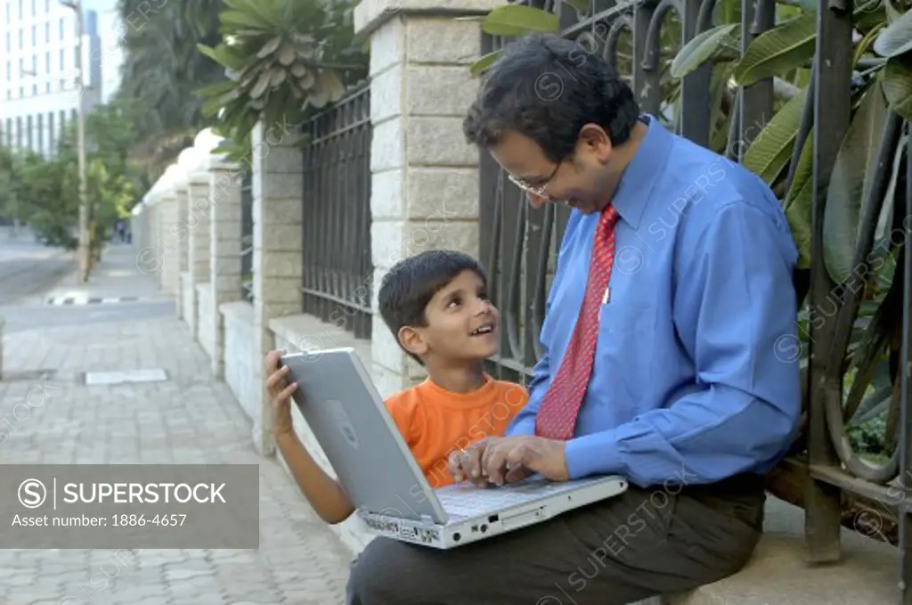 Young Indian Executive father and son on laptop outdoors. Model Release Number 637 and Model Release Number 560.