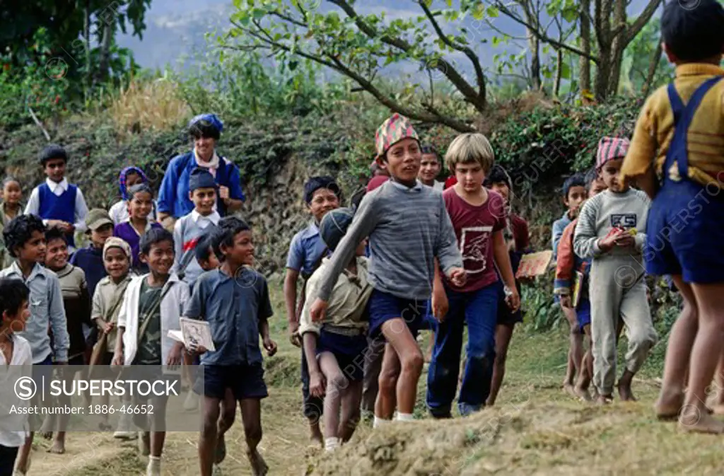 A crowd of VILLAGE BOYS walks with a young TREKKER - ANNAPURNA REGION, CENTRAL NEPAL