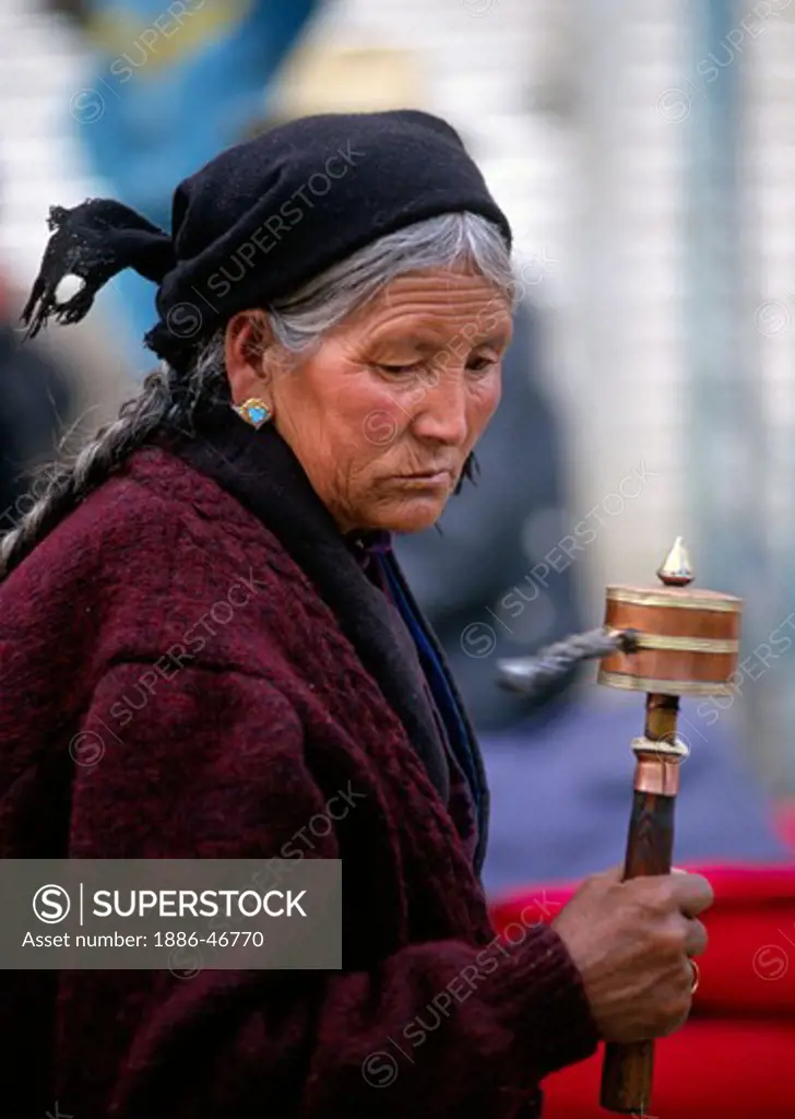 A TIBETAN WOMAN spins her PRAYER WHEEL as she circumambulate the Jokhang Temple along the BARKOR - LHASA, TIBET