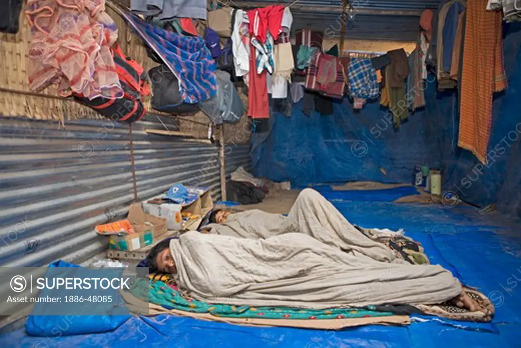 Sick construction workers resting in their temporary corrugated sheet accommodation while their fellow workers are on the work site ; Ahmedabad ; Gujarat ;  India