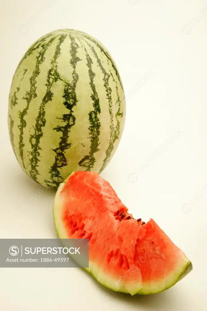 Fruits ; One full watermelon with light and dark green stripes and one cut slice showing red watery pulp with black seeds  ; Pune ;  Maharashtra ; India