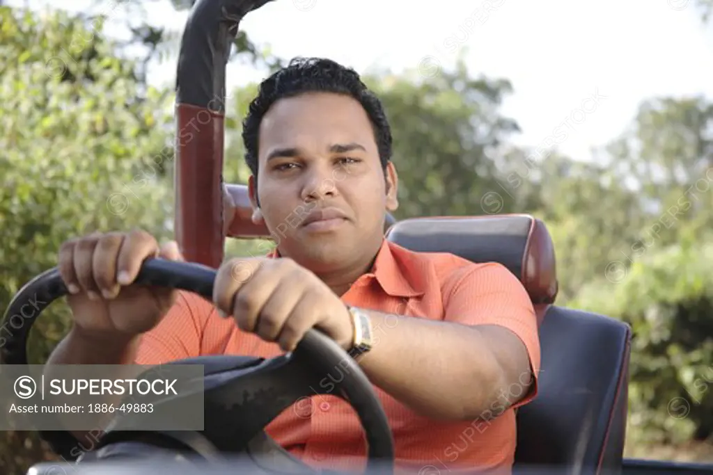 South Asian Indian young man sitting on driver's seat in India jeep and holding steering wheel ; India MR# 703H